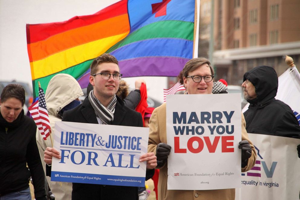 Two people holding signs reading "Liberty and Justice for all" and "Marry who you love"